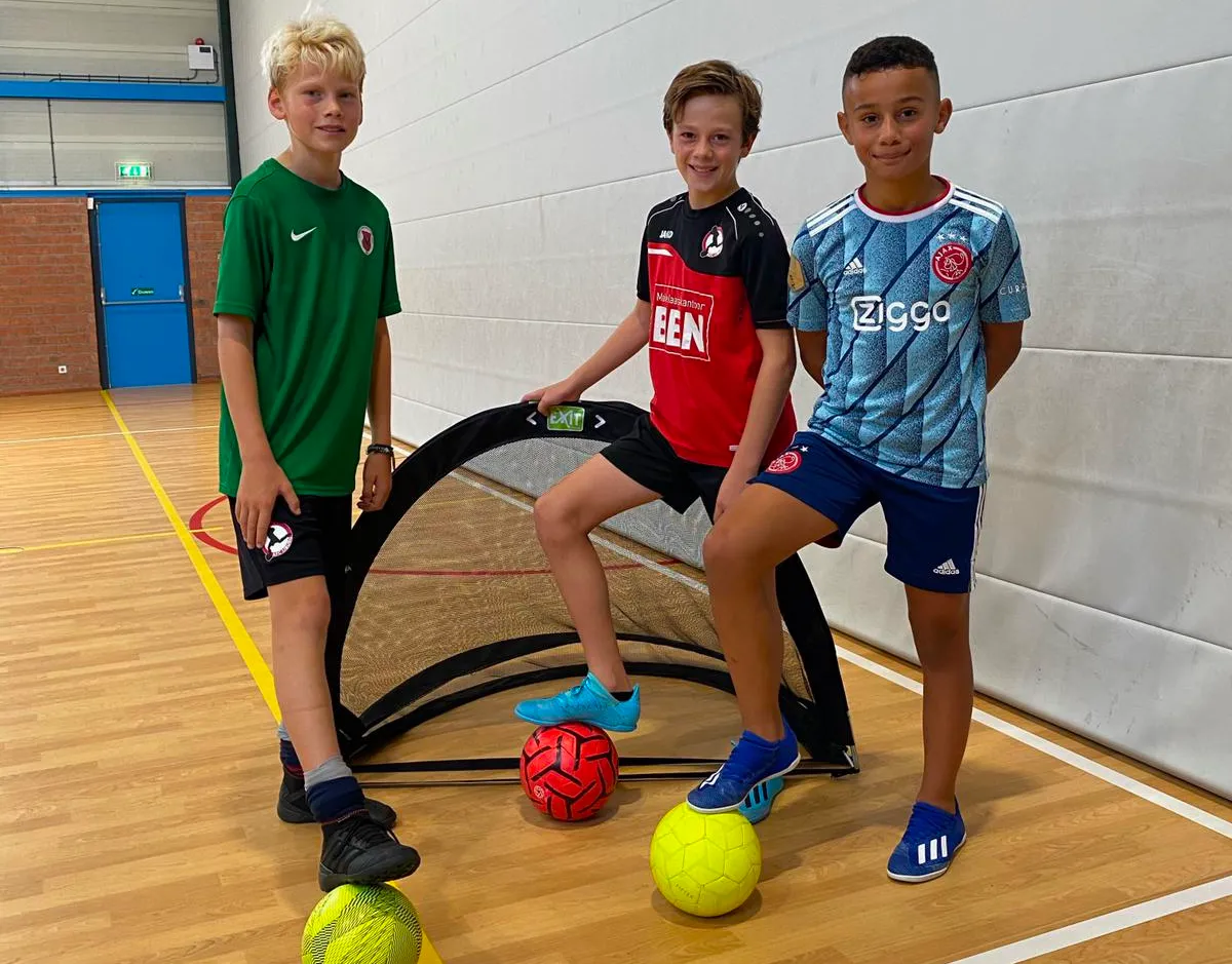 Drie spelers van DPC Academy in clubshirts poseren met ballen in de sporthal.